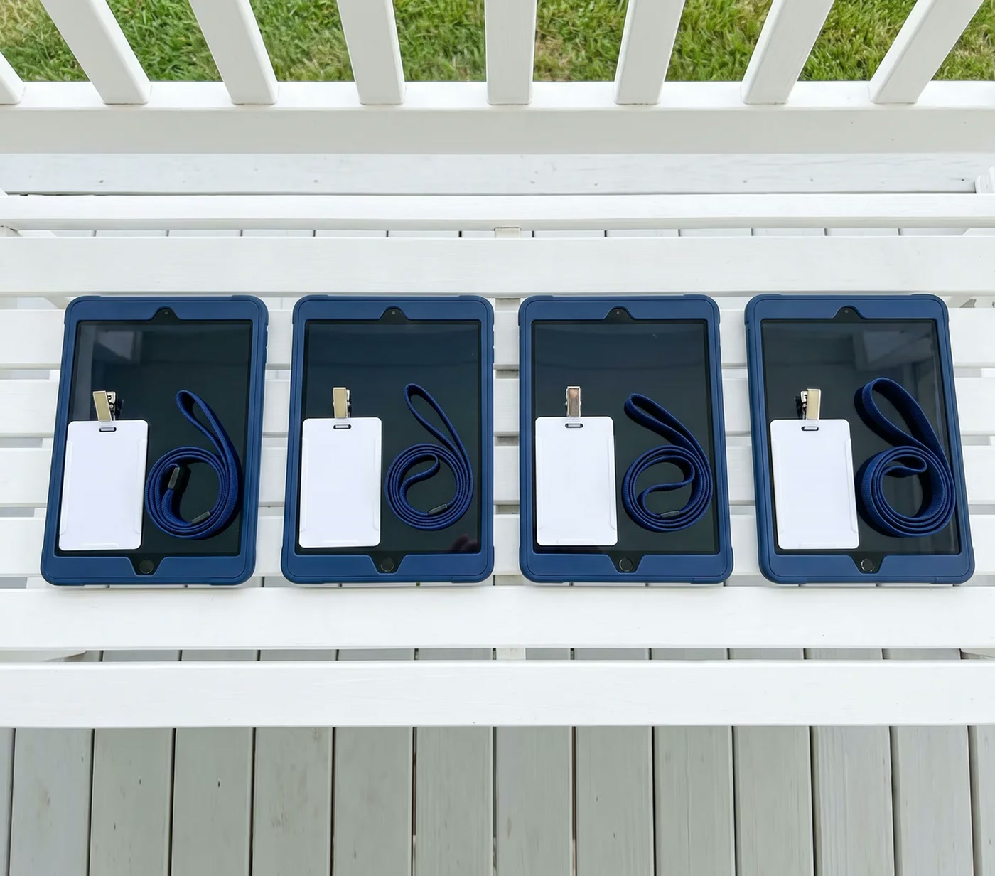 Four matching navy tablets, each with a blank ID badge and lanyard, laid out side by side on a white porch bench